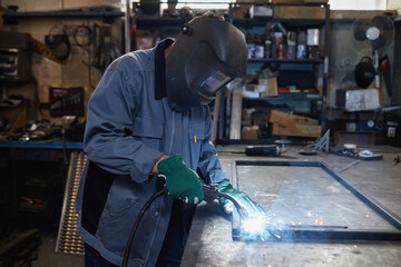 Side view portrait of female welder working with metal in industrial workshop, copy space