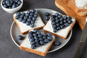 Heart-shaped cream cheese and blueberry sandwiches on rye bread toasts on gray plate