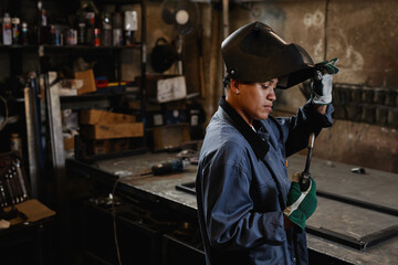 Side view portrait of woman welder inspecting tools in industrial workshop, copy space