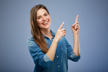 Smiling woman wearing denim shirt pointing finger. Isolated portrait female person on blue.