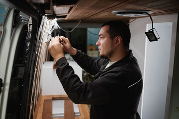 Fototapeta Side view portrait of man building camper van and installing wires for electrics obraz