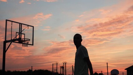 4k video Silhouettes of basketball players at the beautiful sunset. Amazing cinematic sport shoot. Two male playing street ball outside.
