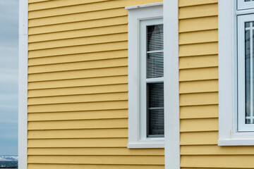 Fototapeta premium The exterior of a bright yellow narrow wooden horizontal clapboard wall of an old house with vinyl windows. The trim on the glass panes is white in color. The outside boards are textured pine wood. 
