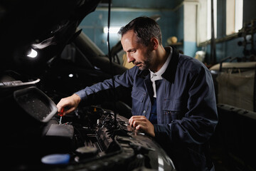 Side view portrait of mature mechanic fixing car engine in dark garage shop