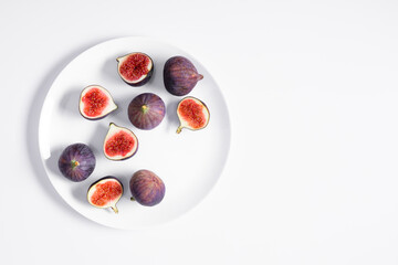 Whole figs and fig sliced in half on plate on white background. Flat lay, top view of fresh ripe sliced figs on table.
