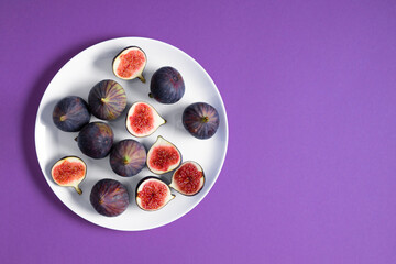 Fresh ripe figs and fig sliced in half on plate on purple background. Flat lay, top view of fresh...