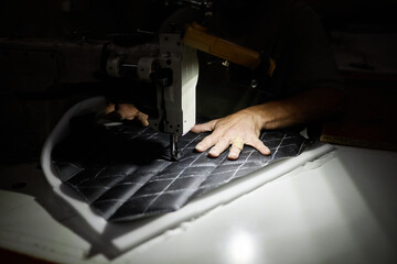 Close up of male worker sewing car upholstery detail with industrial sewing machine in accent light
