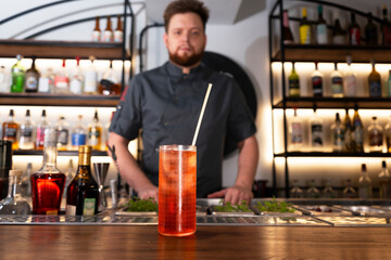 A glass of delicious red alcohol drink with a cocktail tube on a bar counter. Night club drink. Preparing for the party.
