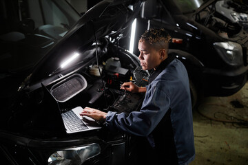 High angle view of female mechanic repairing truck and using laptop in garage with accent light