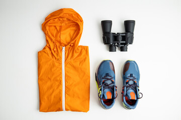 Binoculars, tourist backpack, raincoat on a white background. Top view, flat lay