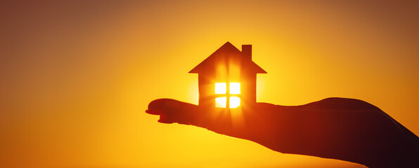 Woman's hand holding a model of a house on sunset evening - 532025690