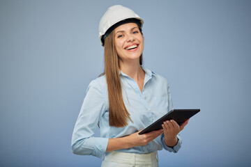 Smiling woman engineer in safety white helmet using digital tablet. Isolated female portrait on blue background.