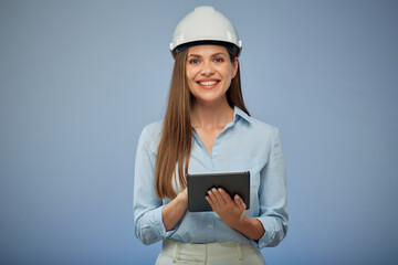 Smiling woman engineer in safety white helmet using digital tablet. Isolated female portrait on blue background. - 532025840