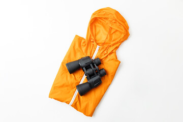 Binoculars lie on an orange cloak on a white background. Top view, flat lay