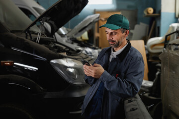 Waist up portrait of mature male worker using smartphone in at car factory workshop