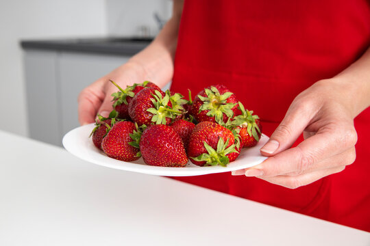 Female hands holding a plate with strawberries in the kitchen