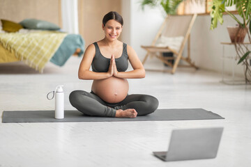 Fototapeta premium Beautiful Pregnant Woman Having Online Yoga Lesson With Laptop At Home