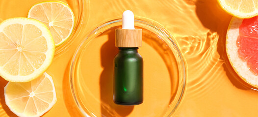 Bottle of citrus essential oil and fruits slices in water on orange background, top view