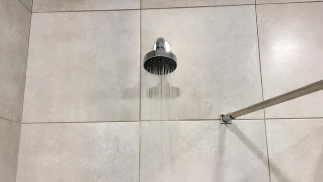 Water flows from the shower metal nozzle and faucet in a modern shower room. A fresh shower with splashes of water in the bathroom. Shower mixer. Block the flow of water in the form of rain