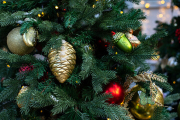 Golden cone Christmas tree toy on a green branch of an artificial Christmas tree, close-up festive sparkling background