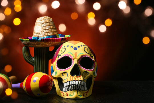 Painted human skull for Mexico's Day of the Dead (El Dia de Muertos), maracas, cactus and sombrero on dark background