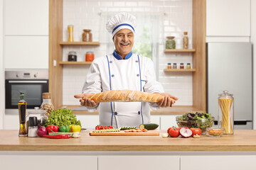 Cheerful mature male chef holding a bread behind a kitchen counter
