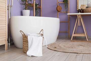 Basket with towel near modern bathtub in stylish bathroom interior