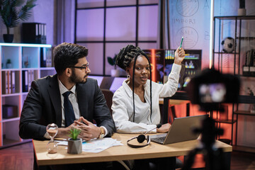 Attractive male and female financiers, arab manager and confident african american business woman explaining online economic charts on glass board to their colleagues sitting in front of video camera.