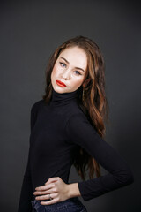 A brunette in black clothes, with bright make-up, against the background of a dark wall