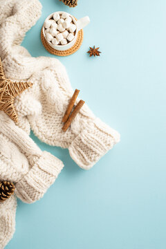 Winter holidays concept. Top view vertical photo of white knitted sweater cup of cocoa with marshmallow on placemat rattan star pine cones anise and cinnamon sticks on isolated pastel blue background