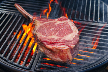 Barbecue dry aged wagyu tomahawk steak offered as close-up on a charcoal grill with fire and smoke