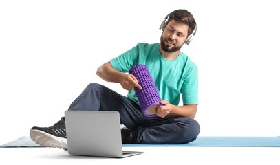 Young man with headphones, foam roller and laptop on white background