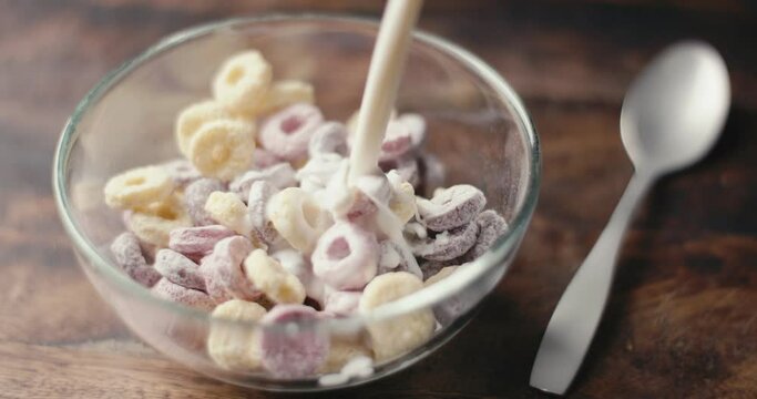 Milk or yogurt pours on cereal bowl breakfast food table in close up