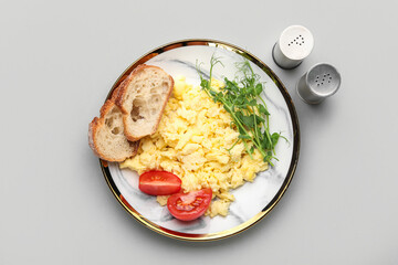 Plate of tasty scrambled eggs, tomatoes, bread, green sprouts and spices on light background