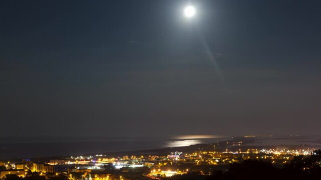 Time lapse shot of the moving moon and stars over the city of Bastia. The Mediterranean Sea in the background reflects the moonlight.