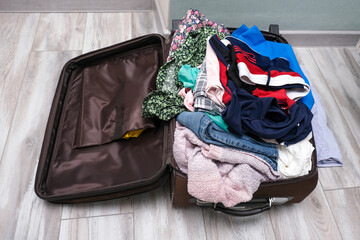 Open suitcase on the floor with a messy pile of clothes, overload baggage, traveling concept