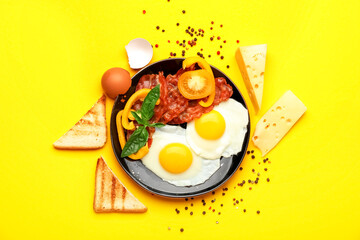 Composition with plate of tasty fried eggs, bacon, toasts and cheese on yellow background