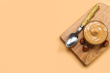 Wooden board with bowl of tasty hazelnut butter on color background