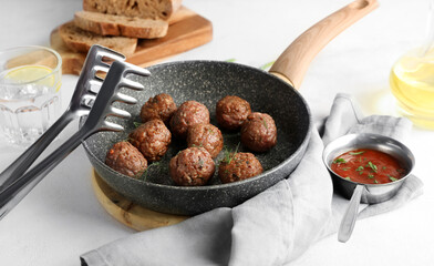 Frying pan with meat balls, tongs, sauce and napkin on white background