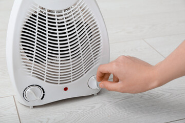 Woman adjusting electric fan heater on floor