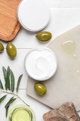 Boards with jar of cream, green olives, oil and plant branch on white wooden background
