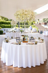 Table decoration with white flowers for guests in a restaurant. Beautifully decorated tables for a banquet in a restaurant overlooking the park. Preparing for a wedding party. Beautiful wedding decor