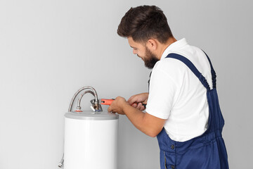 Male plumber repairing boiler with pipe wrench in bathroom