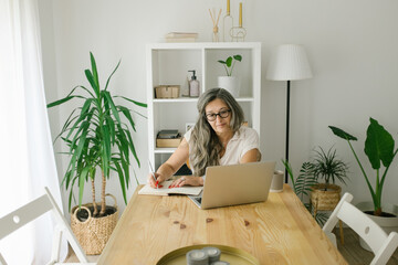 Woman writing notes in notebook from online meeting