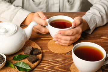 Female hands with cups of hot puer tea on wooden background, closeup