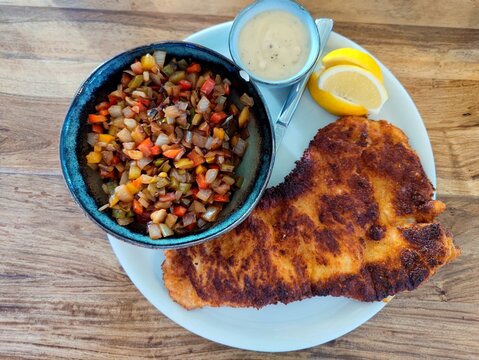 Delicious Crispy Fried Wiener Schnitzel With A Bowl Of Fried Onion, Bell Pepper And Mushrooms And Pepper Sauce On A Restaurant Table. There Are No People Or Trademarks In The Shot.