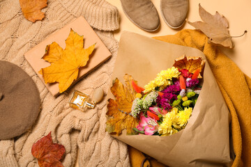 Stylish female clothes, accessories, bouquet of flowers and autumn leaves on beige background