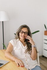 Lifestyle portrait of a happy woman sitting and talking on the phone at home