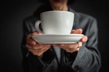 a girl in a hat and a gray jacket holds a white cup with morning coffee and tea in her hands, on a gray background. Selective focus