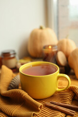 Cup of hot tea, sweater, candle and pumpkins on the windowsill, autumn atmosphere
